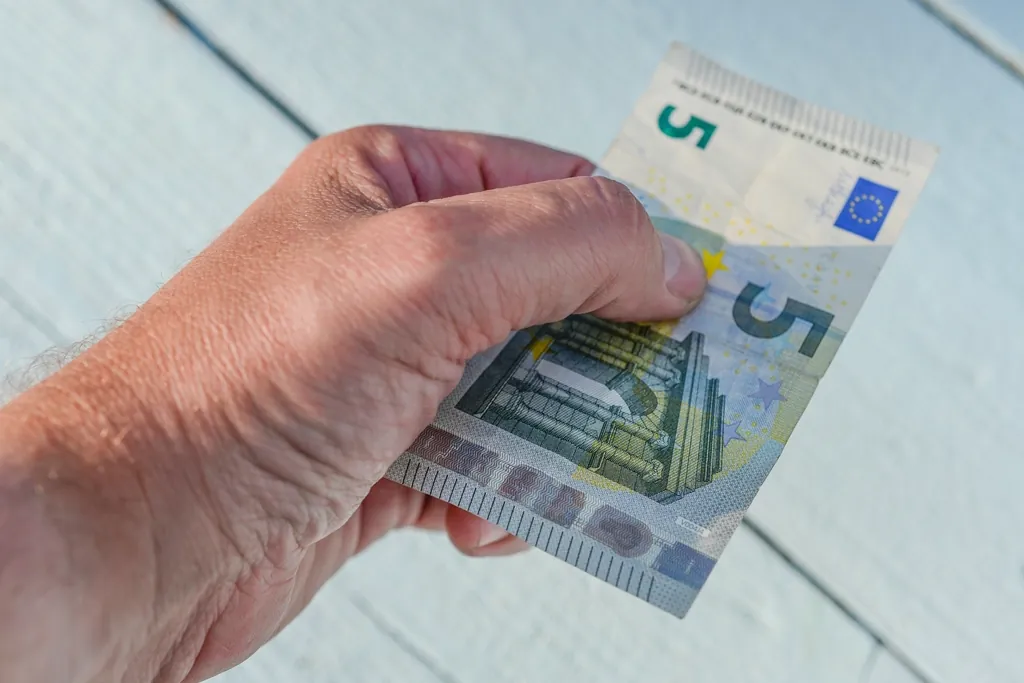 Main qui tient quelques billets de 5 euros au-dessus d'une table blanche.