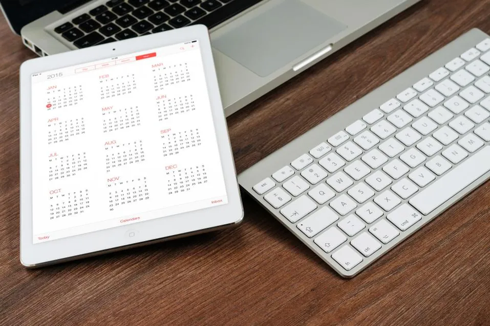 Tablette affichant un calendrier annuel, posée sur un bureau en bois à côté d'un clavier.