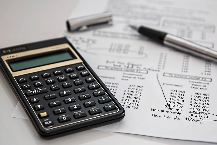 Calculatrice et stylo posés sur des feuilles couvertes de colonnes de chiffres.