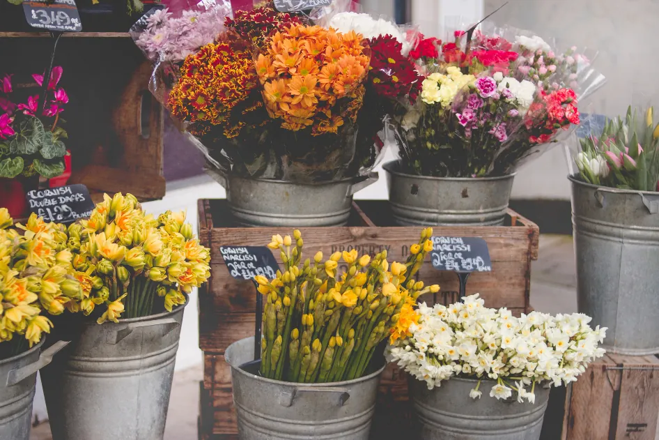 Étal de fleuriste : seaux en zinc remplis de bouquets jaunes, orange et roses.