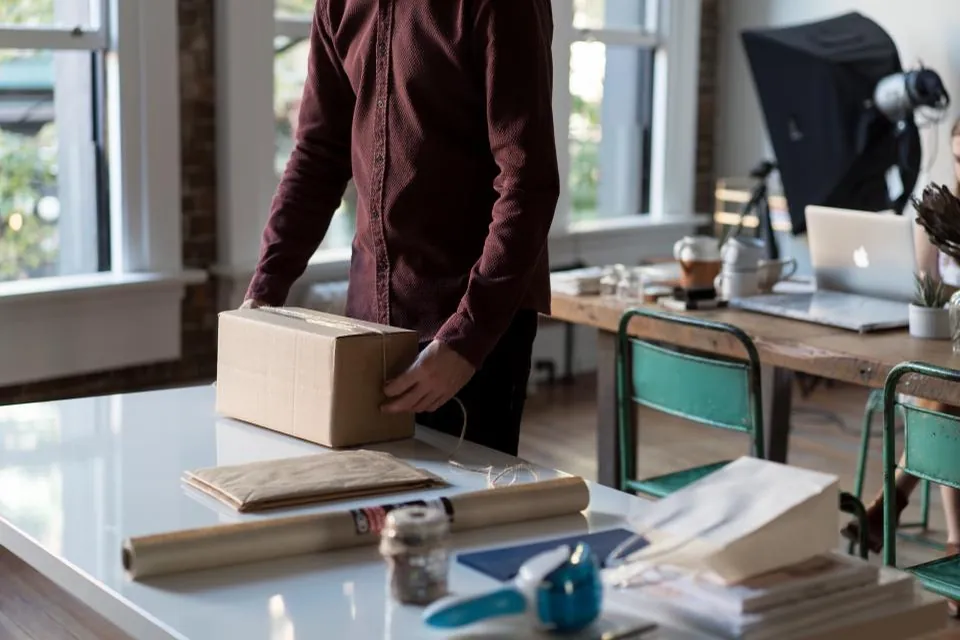 Personne qui ferme un carton sur une table encombrée de papier d'emballage.