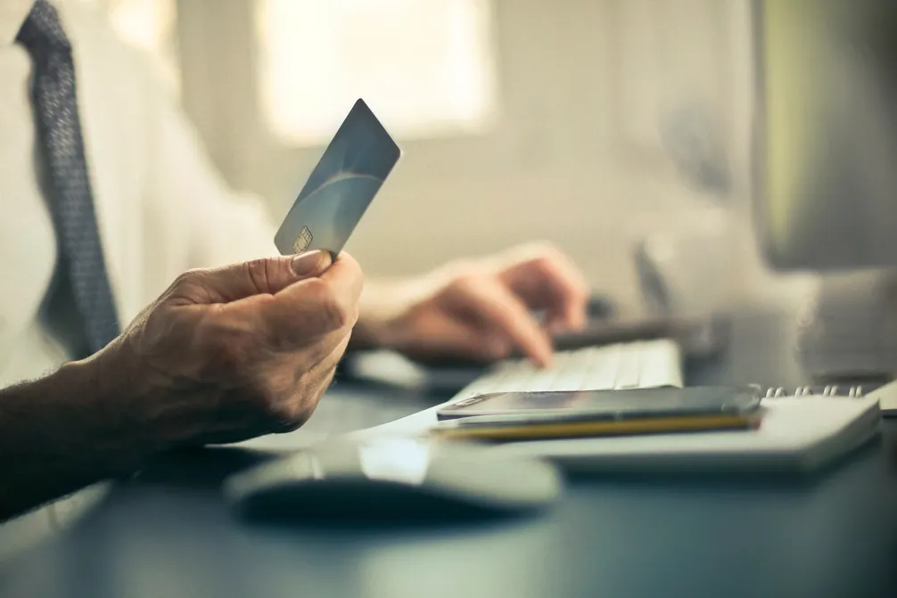 Main qui tient une carte bancaire au-dessus d'un bureau, clavier d'ordinateur à côté.