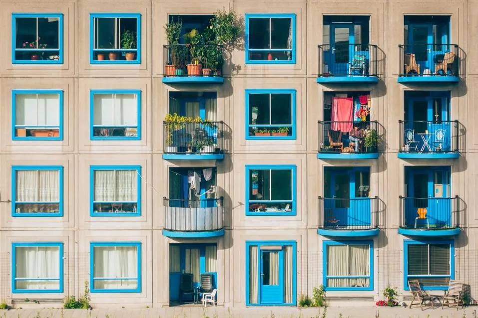 Façade d'immeuble aux fenêtres encadrées de bleu, balcons garnis de plantes.
