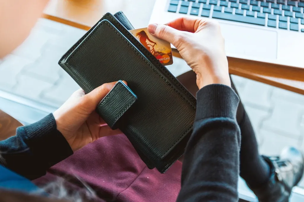 Personne assise devant un ordinateur portable qui sort une carte bancaire de son portefeuille.