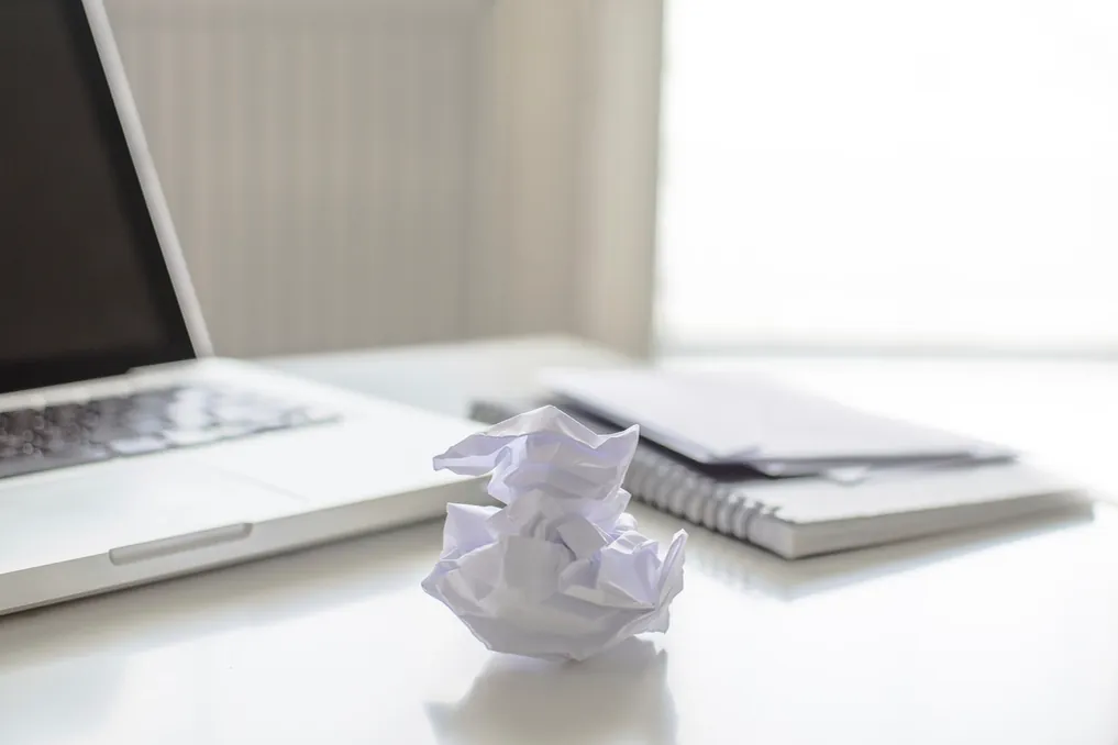 Ordinateur portable, bloc de papier et feuille froissée en boule sur un bureau clair.