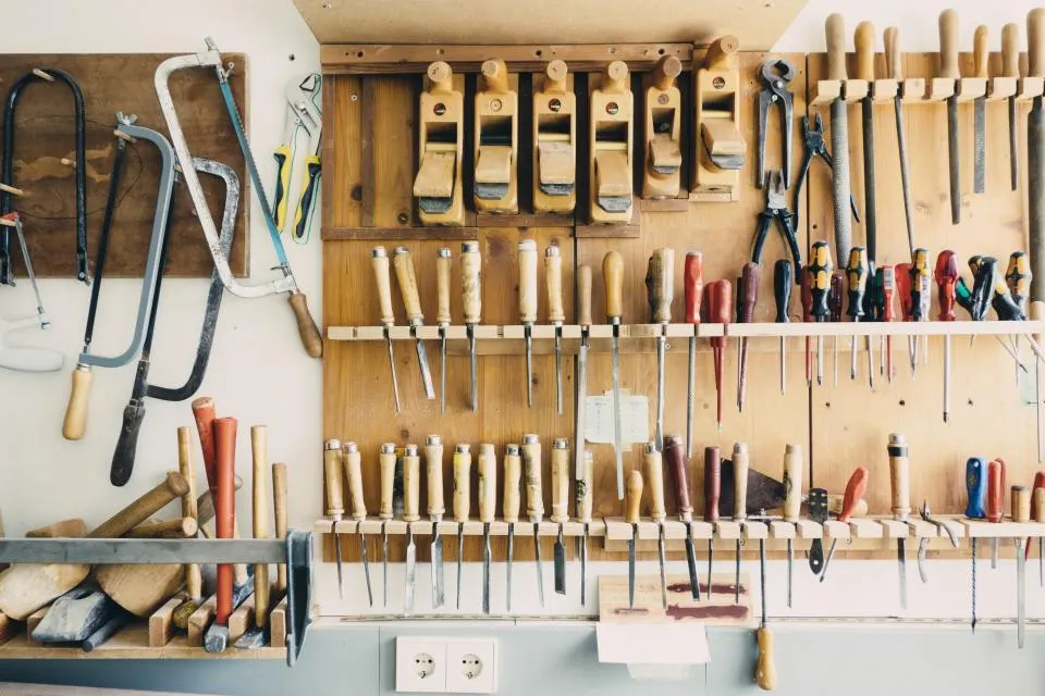Mur d'atelier couvert d'outils à main rangés sur des étagères en bois : scies, rabots, ciseaux et tournevis.