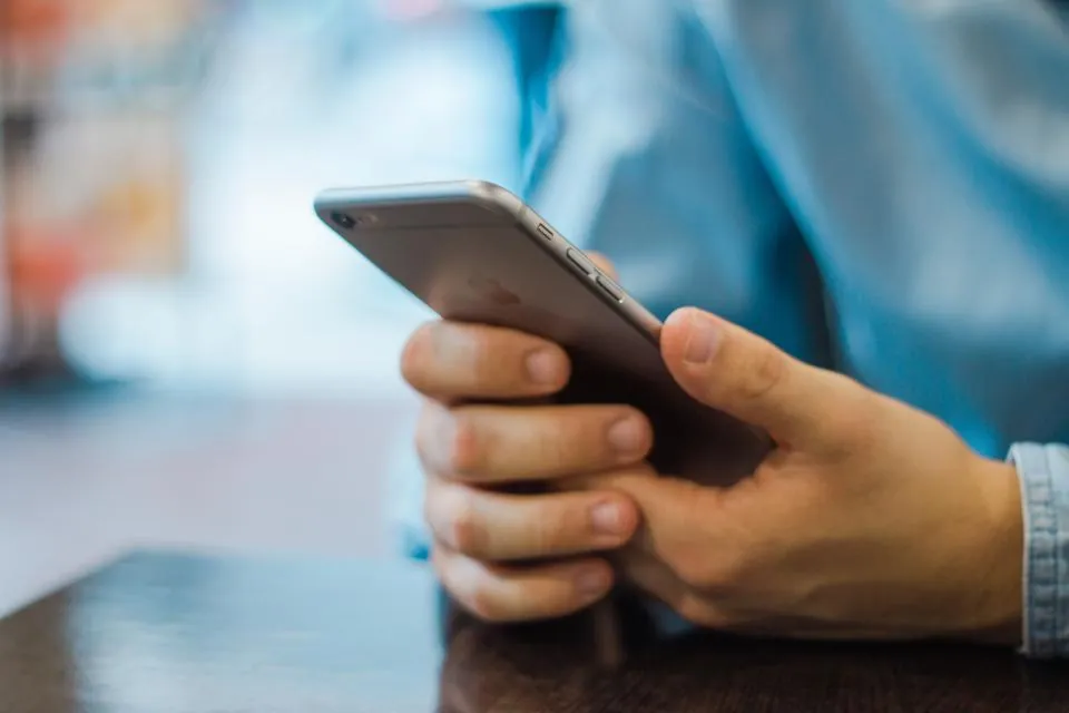 Mains qui tiennent un smartphone, avant-bras posés sur une table.