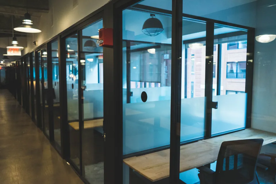 Couloir de bureaux vitrés, vide, une chaise seule dans une salle de réunion.