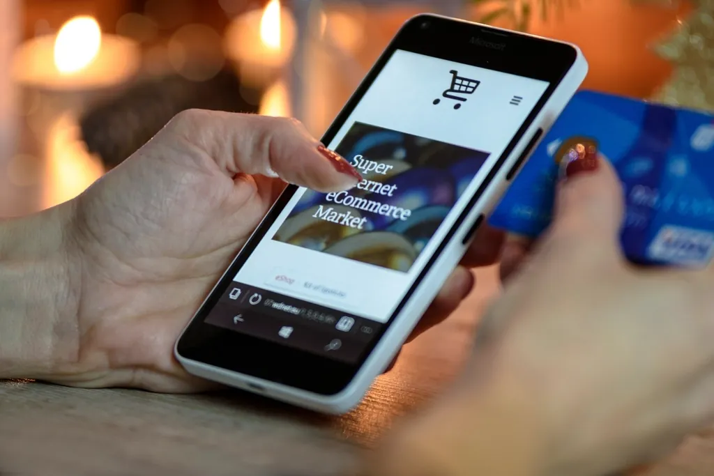 Mains tenant un smartphone ouvert sur une boutique en ligne, carte bancaire dans l'autre main.